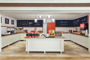 A modern kitchen with white cabinets, a central island with coffee machines, and a chalkboard wall with kitchen-related drawings.