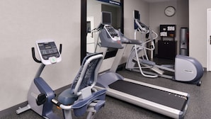 Ein Fitnessraum mit Laufbändern, Crosstrainern und einer Spiegelwand.