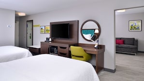 Ein Hotelzimmer mit zwei Betten, einem Schreibtisch, einem Flachbildfernseher, einer Mikrowelle und einer kleinen Sitzecke mit Sofa und Sessel.