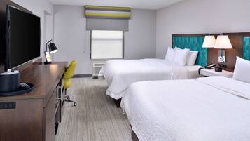 A hotel room with two beds, a desk with a computer, a TV, and a window with blinds.