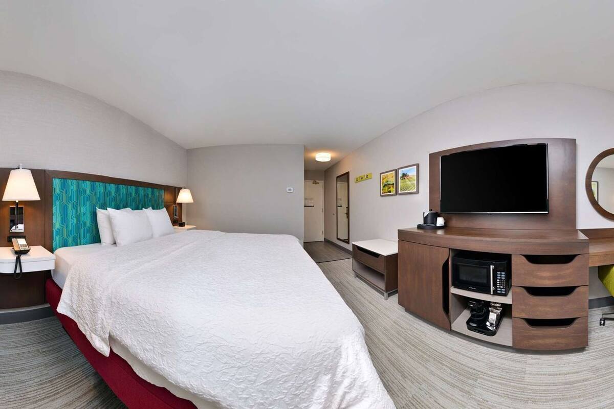 A hotel room with a bed, a sofa, a desk with a TV, a mirror, and a microwave.