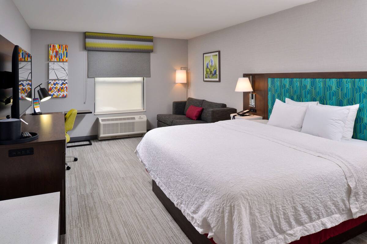 A hotel room with a large bed, a desk with a computer, a sofa, and a TV.