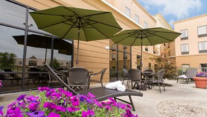 A hotel patio with outdoor seating, including chairs and tables, and green umbrellas providing shade. - Hampton Inn & Suites Springboro/Dayton Area South (Springboro)