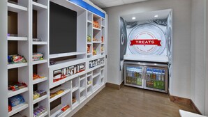 A snack bar with shelves stocked with various packaged snacks and a refrigerated display case. - Hampton Inn & Suites Springboro/Dayton Area South (Springboro)