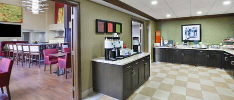 A modern kitchen with a checkered floor, a coffee station, and a dining area with red chairs.