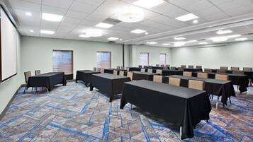 A conference room with tables and chairs, a projector screen, and windows with blinds.
