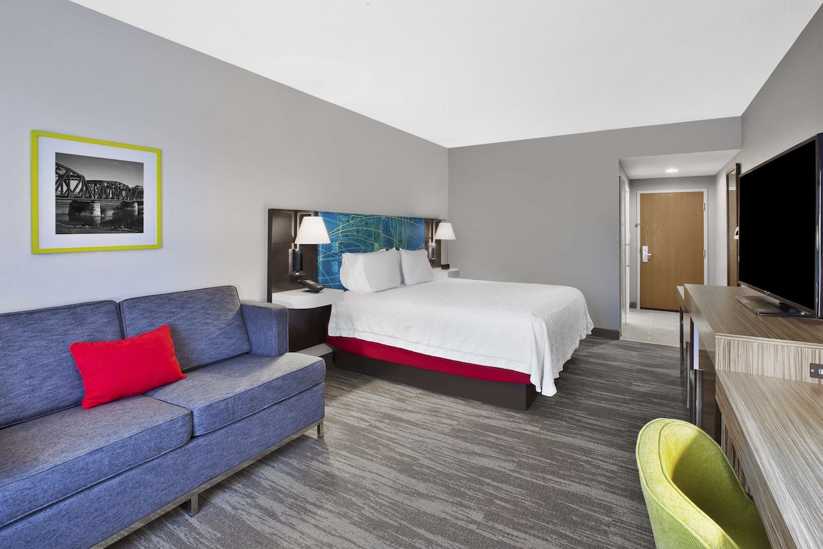 Une chambre d’hôtel avec un lit, un canapé, un bureau, une télévision et un tableau au mur.