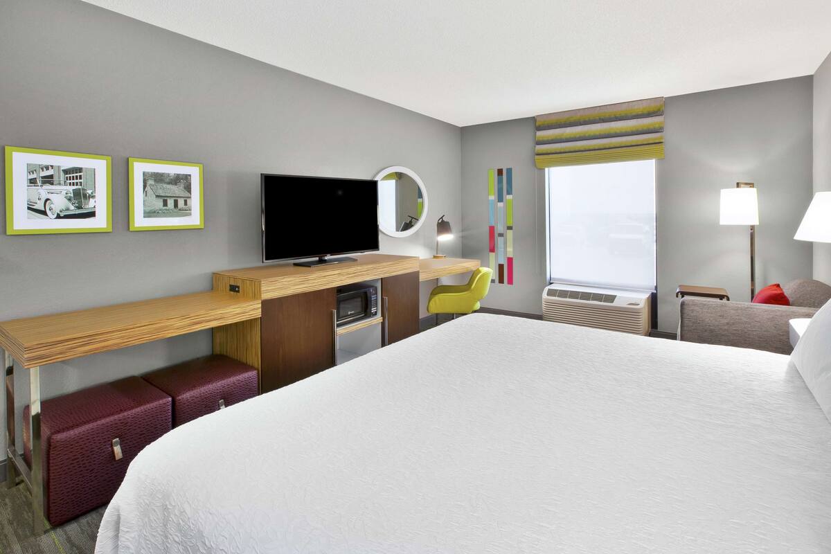 Une chambre d’hôtel dotée d’un grand lit, d’un bureau avec un téléviseur à écran plat, d’un micro-ondes et d’un petit coin salon avec un fauteuil.