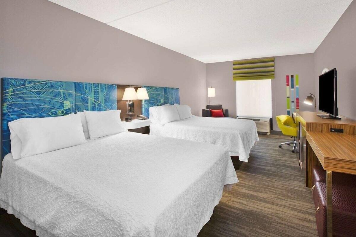 Une chambre d’hôtel avec deux lits, un bureau, une télévision et une fenêtre avec des rideaux.