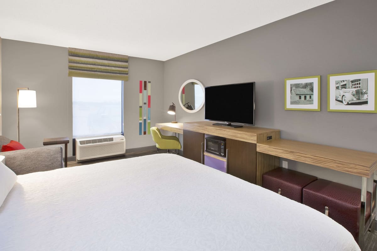 Une chambre d’hôtel avec un grand lit, un bureau avec un ordinateur, une télévision, une fenêtre donnant sur un beau paysage et un four à micro-ondes.