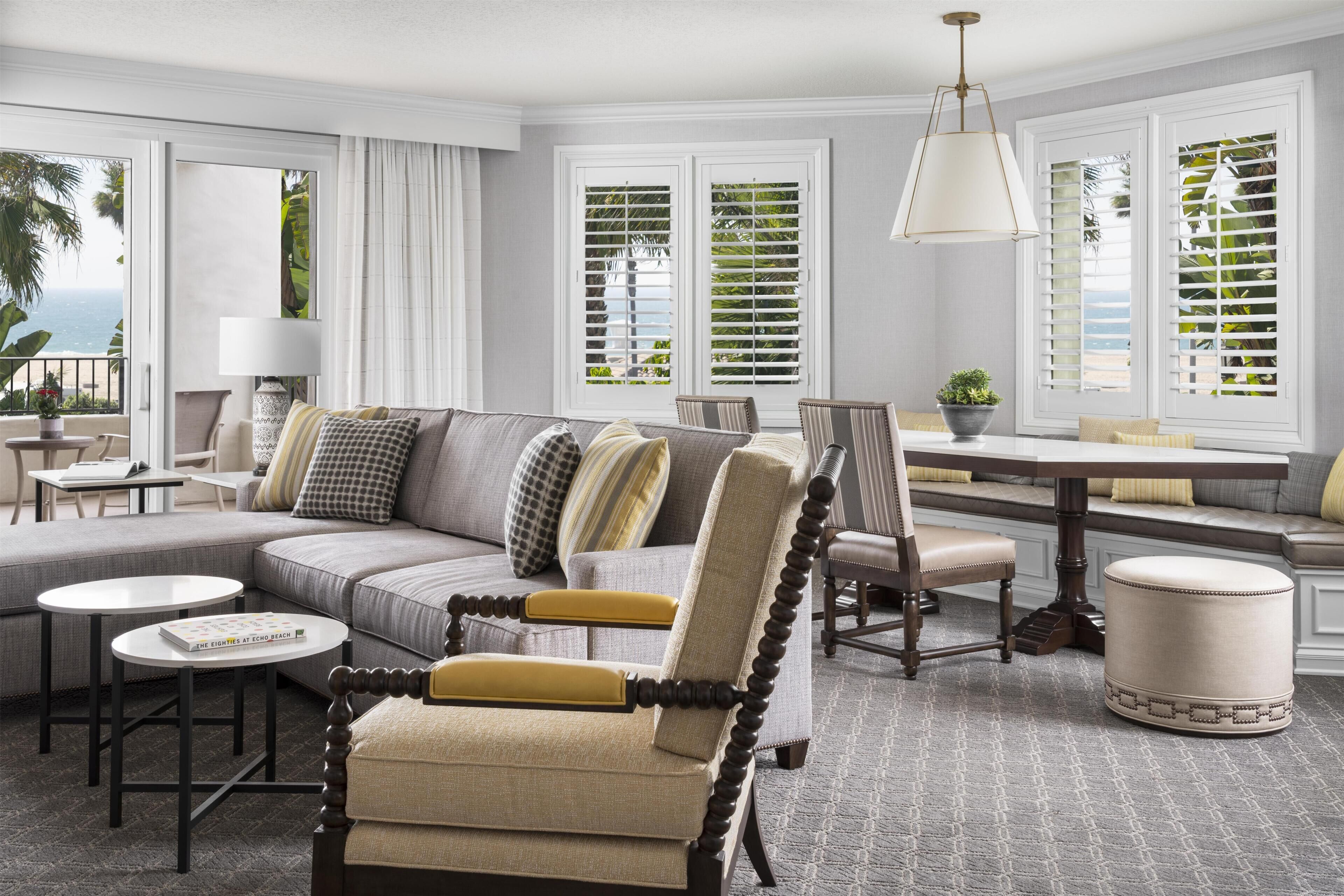 A spacious living room with a large sectional sofa, a wooden armchair, a dining table, and a view of the ocean through the windows.