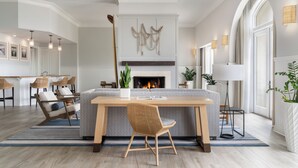 A modern living room with a fireplace, a dining area with wicker chairs, and a large window providing natural light.
