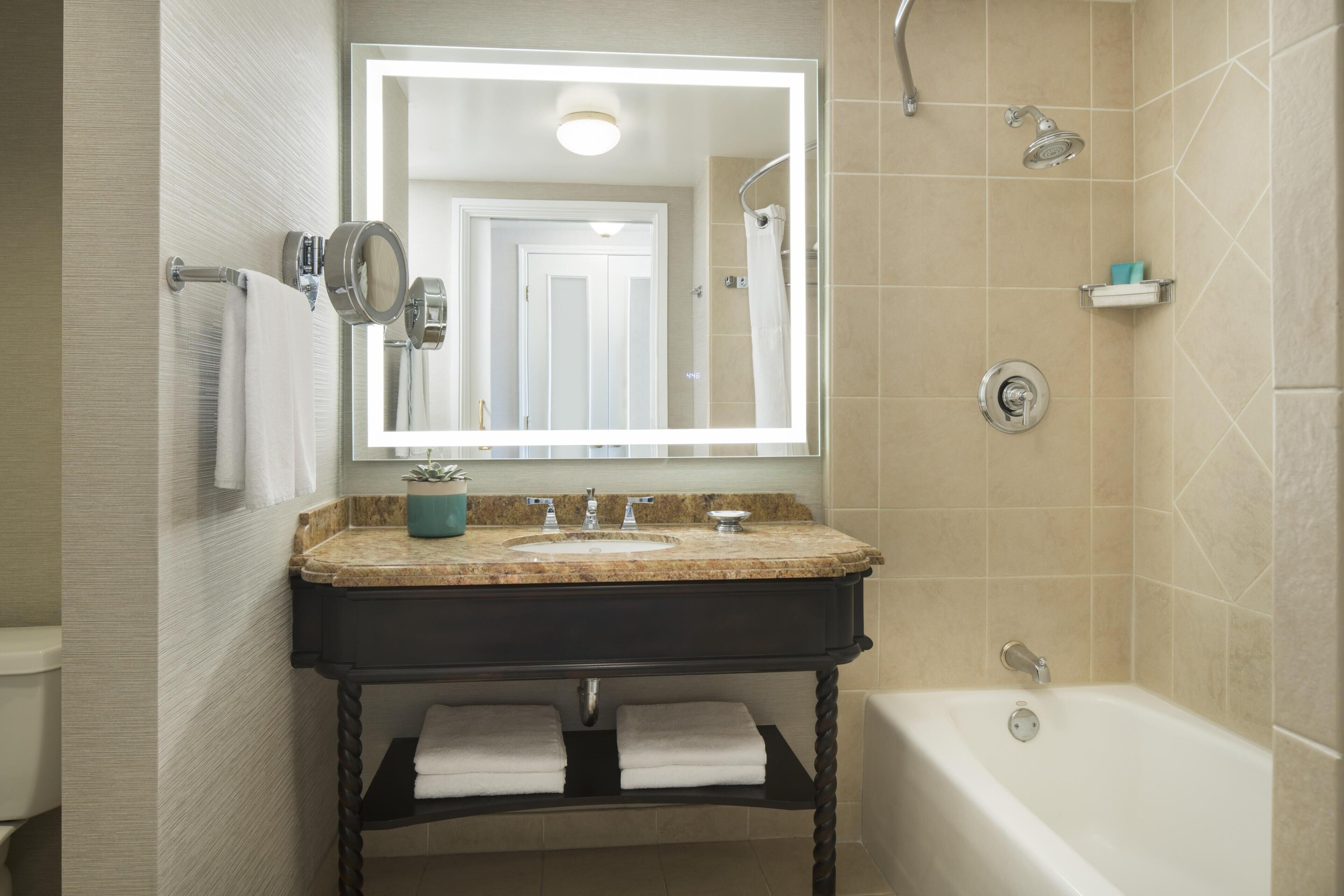 A bathroom with a double sink vanity, a large mirror, a bathtub, and a shower.