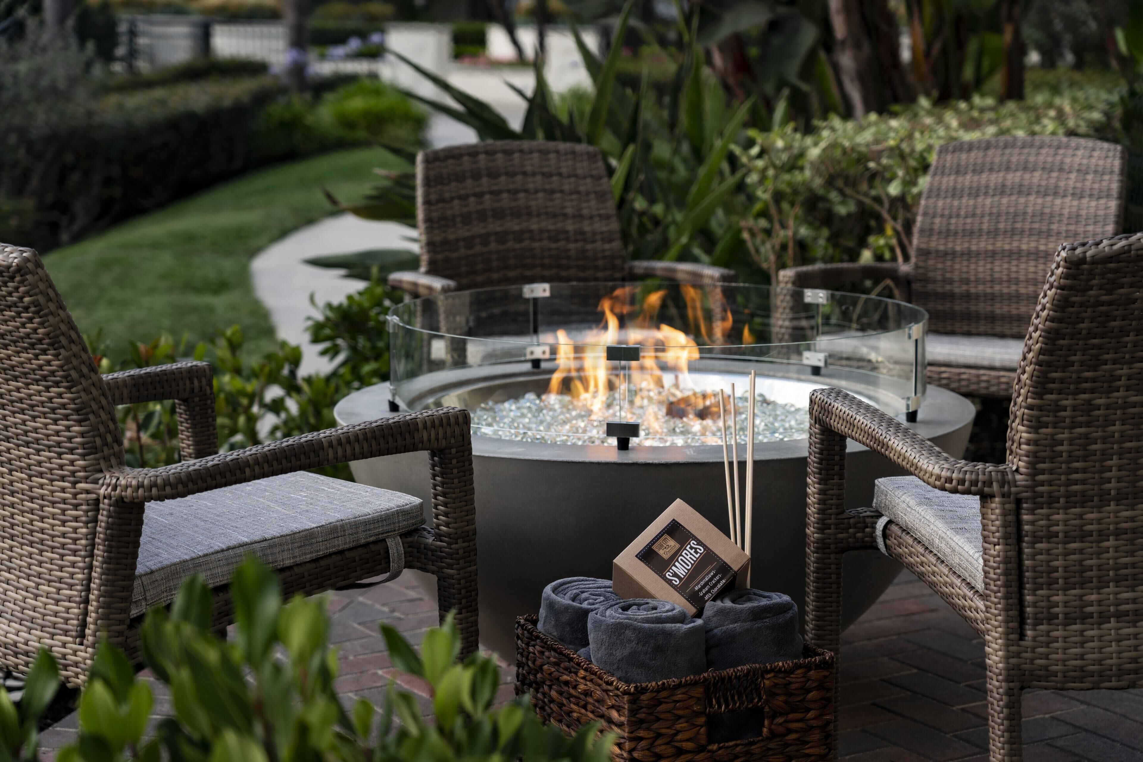 A fire pit surrounded by wicker chairs and a basket of items.