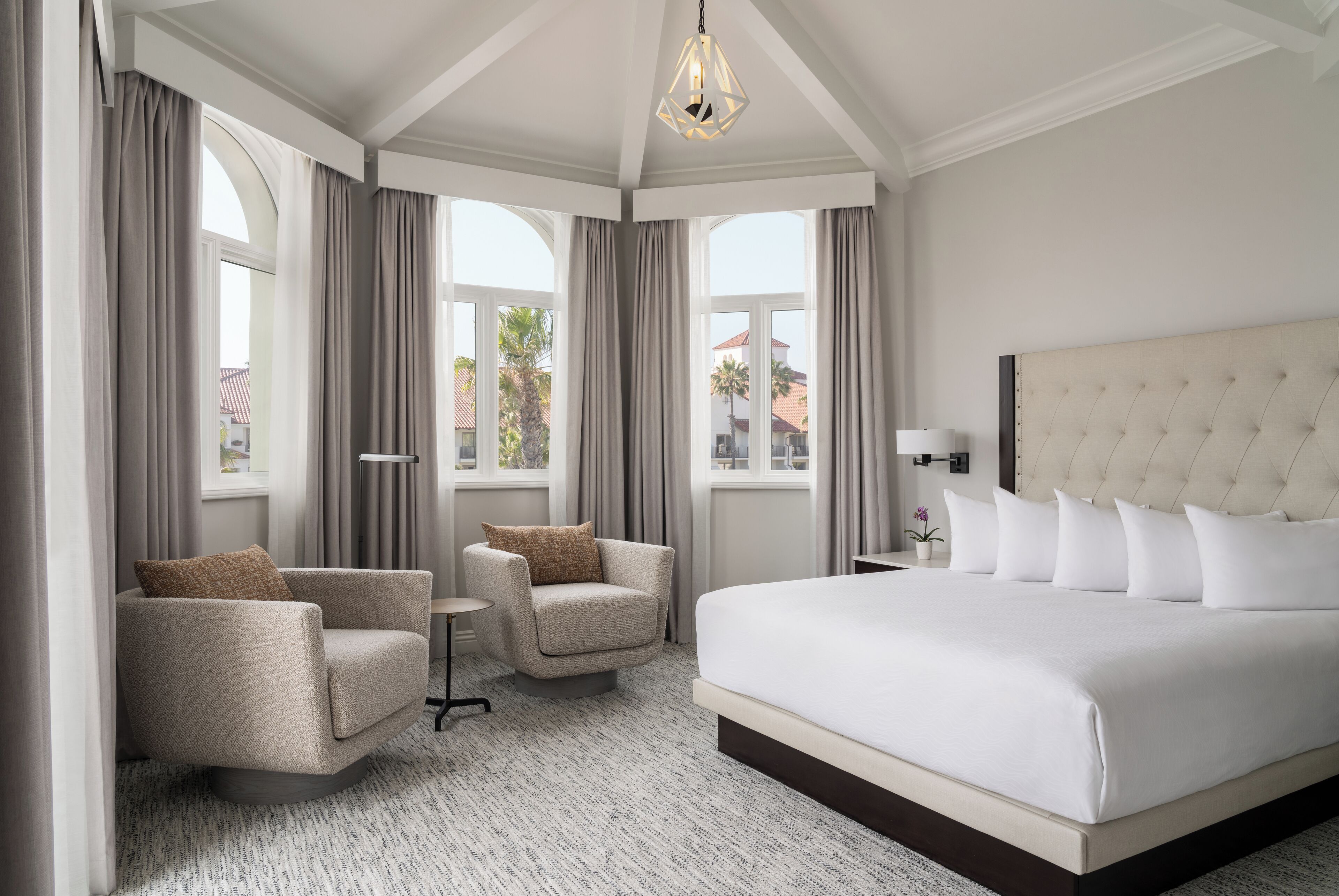 A hotel room with a large bed, two armchairs, a small table, and a lamp.