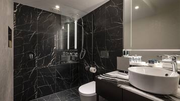 A modern bathroom with a black marble wall, a white sink, and a glass-enclosed shower.