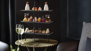 A three-tiered dessert display on a round table with a woven coaster, accompanied by two glasses of white wine. - Fable Dunedin (Dunedin)