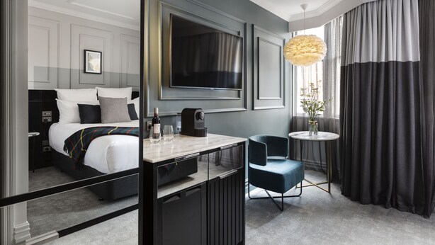 A modern hotel room with a bed, a desk, a chair, a TV, and a large window with curtains. - Fable Dunedin (Dunedin)