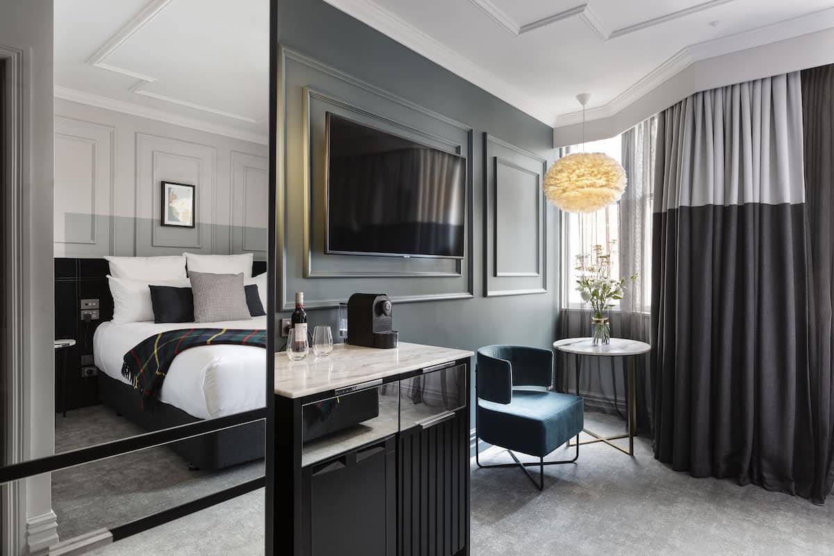 A modern hotel room with a bed, a desk, a chair, a TV, and a large window with curtains.