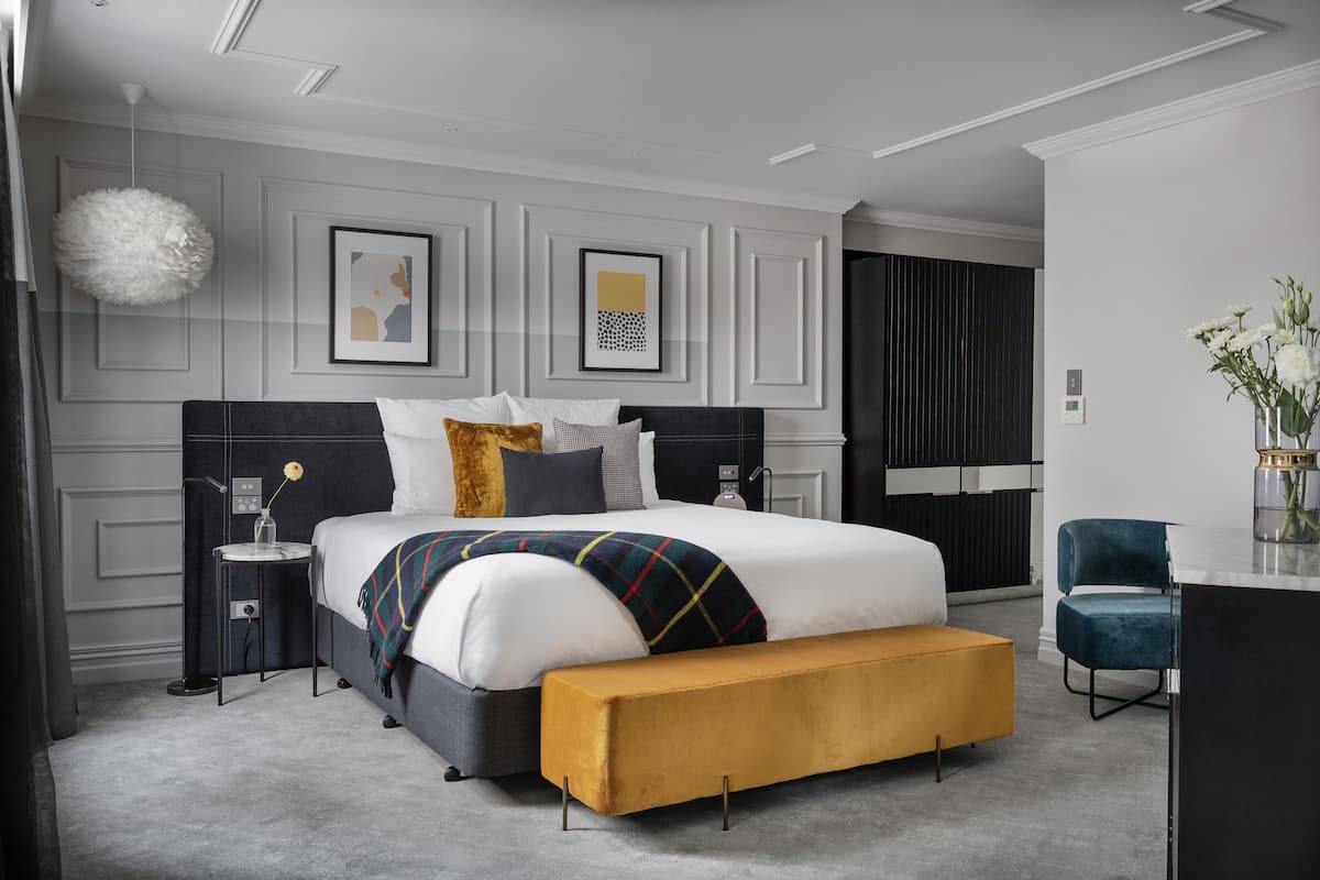 A modern bedroom with a large bed, bedside tables, a bench, and artwork on the walls.