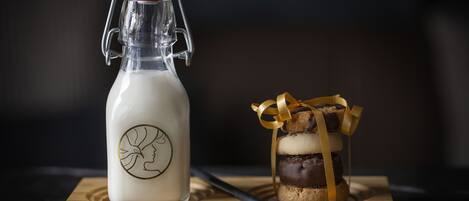 A milk bottle with a red cap and a handle, a wooden cutting board, and a stack of layered cookies with a ribbon.