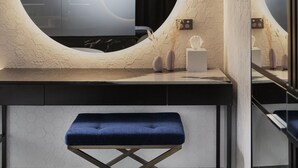 A modern bathroom with a round mirror, a vanity with a marble countertop, and a blue bench. - Fable Dunedin (Dunedin)