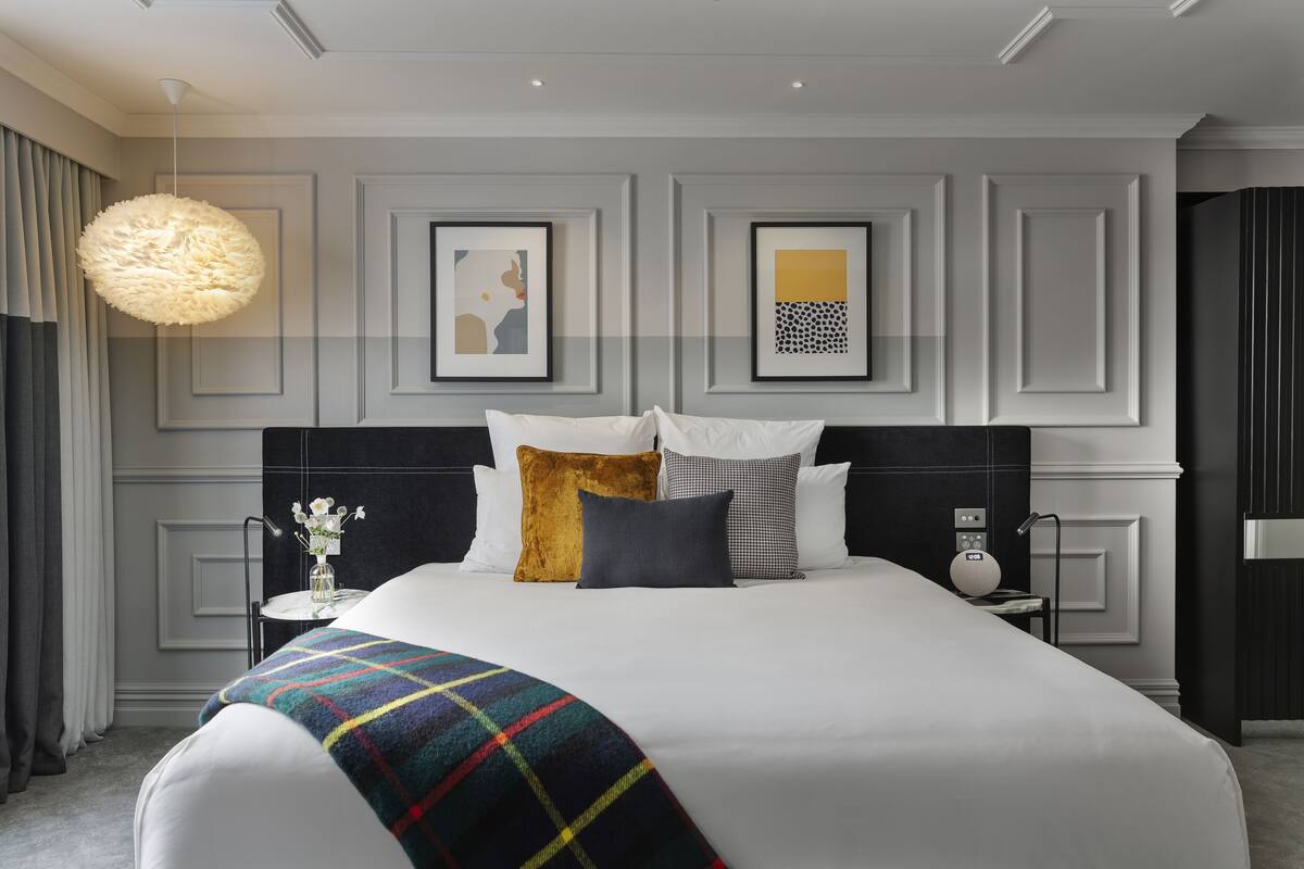 A modern hotel room with a large bed, a bedside table with a lamp, and artwork on the wall.
