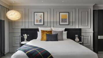 A modern hotel room with a large bed, a bedside table with a lamp, and artwork on the wall.