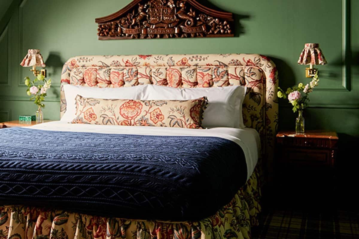 A bedroom with a bed, green walls, a decorative headboard, and floral-patterned bedding.