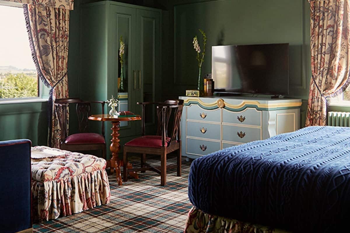 A room with a bed, a dresser, a chair, a table, and a television.