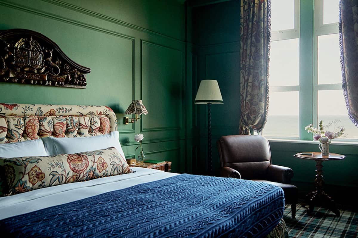 A hotel room with a large bed, a chair, a lamp, and a window with curtains.