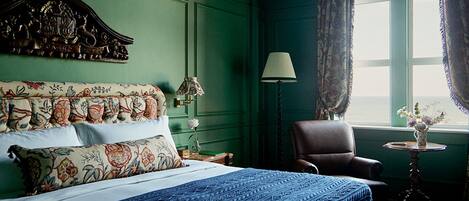 Una habitación de hotel con una cama grande, una silla, una lámpara y un ventanal con cortinas.