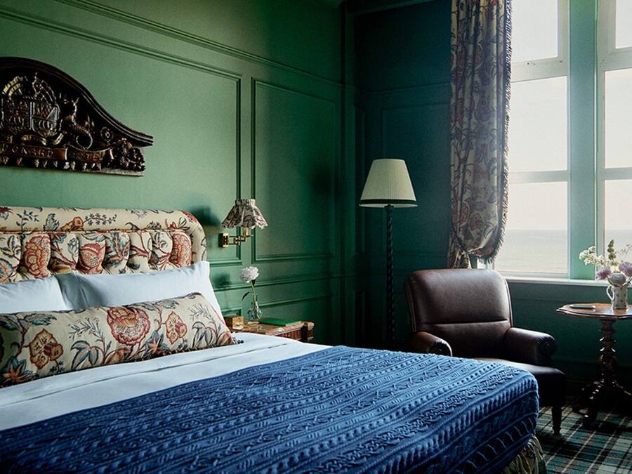 A hotel room with a large bed, a chair, a lamp, and a window with curtains.