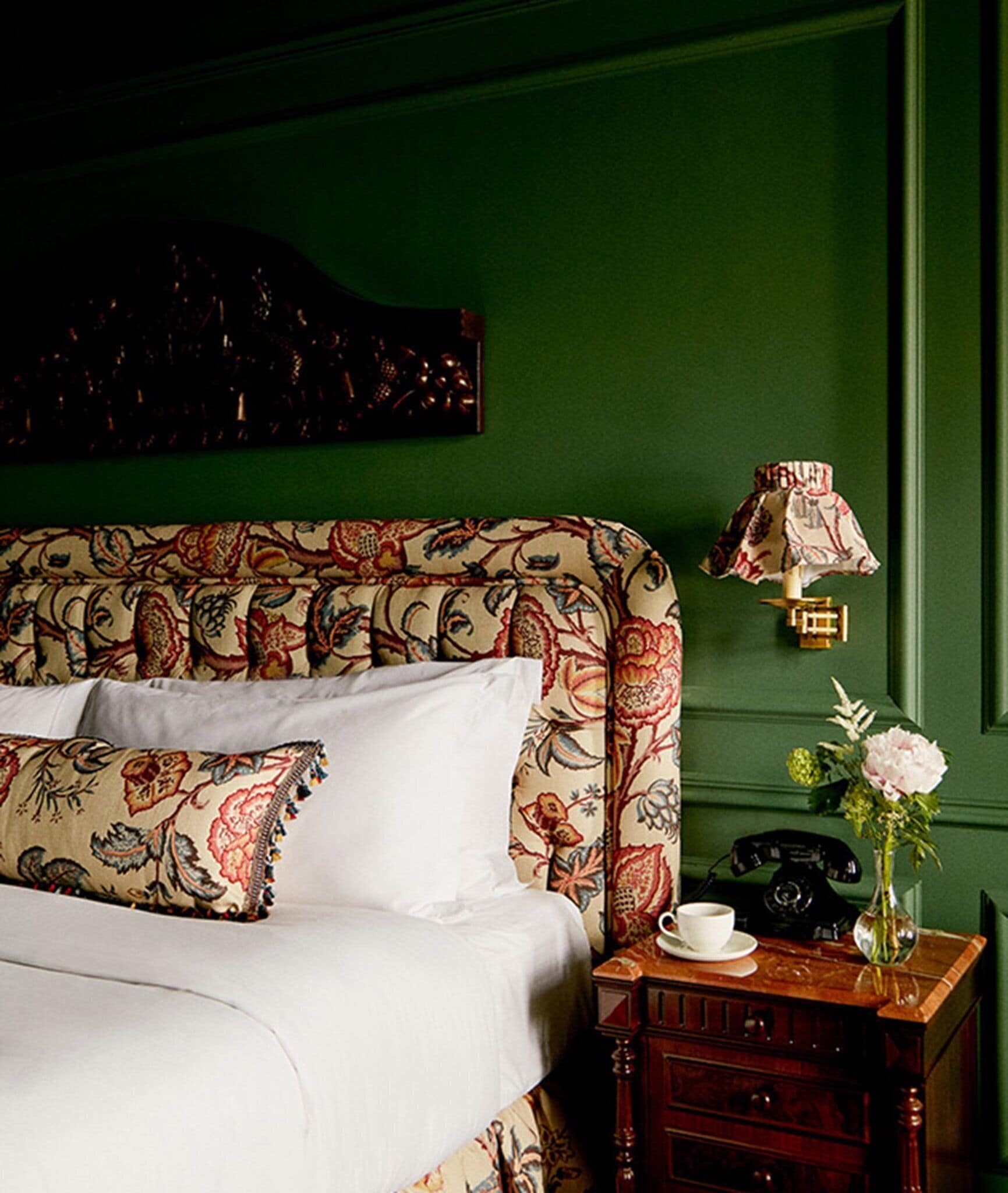 A bedroom with a bed, a nightstand, a telephone, and a vase with flowers.
