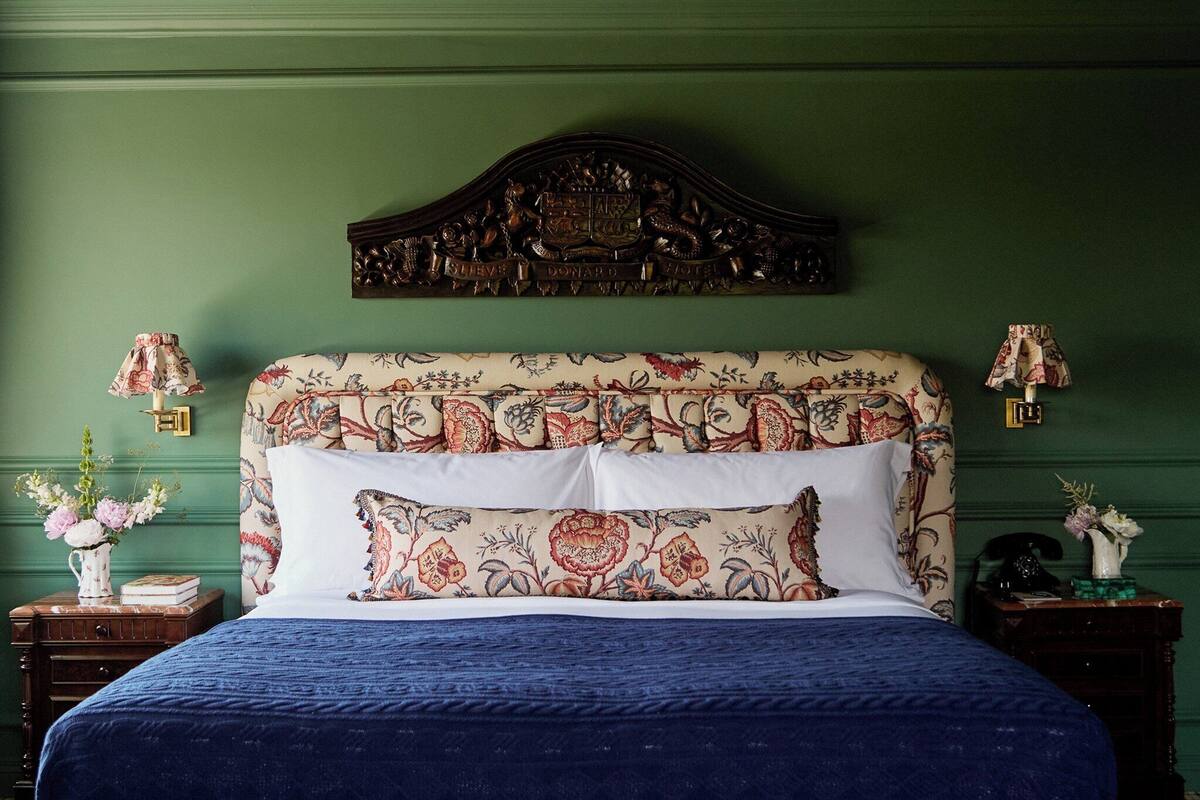 A bedroom with a floral-patterned headboard, a blue bedspread, and two bedside tables with lamps and floral arrangements.