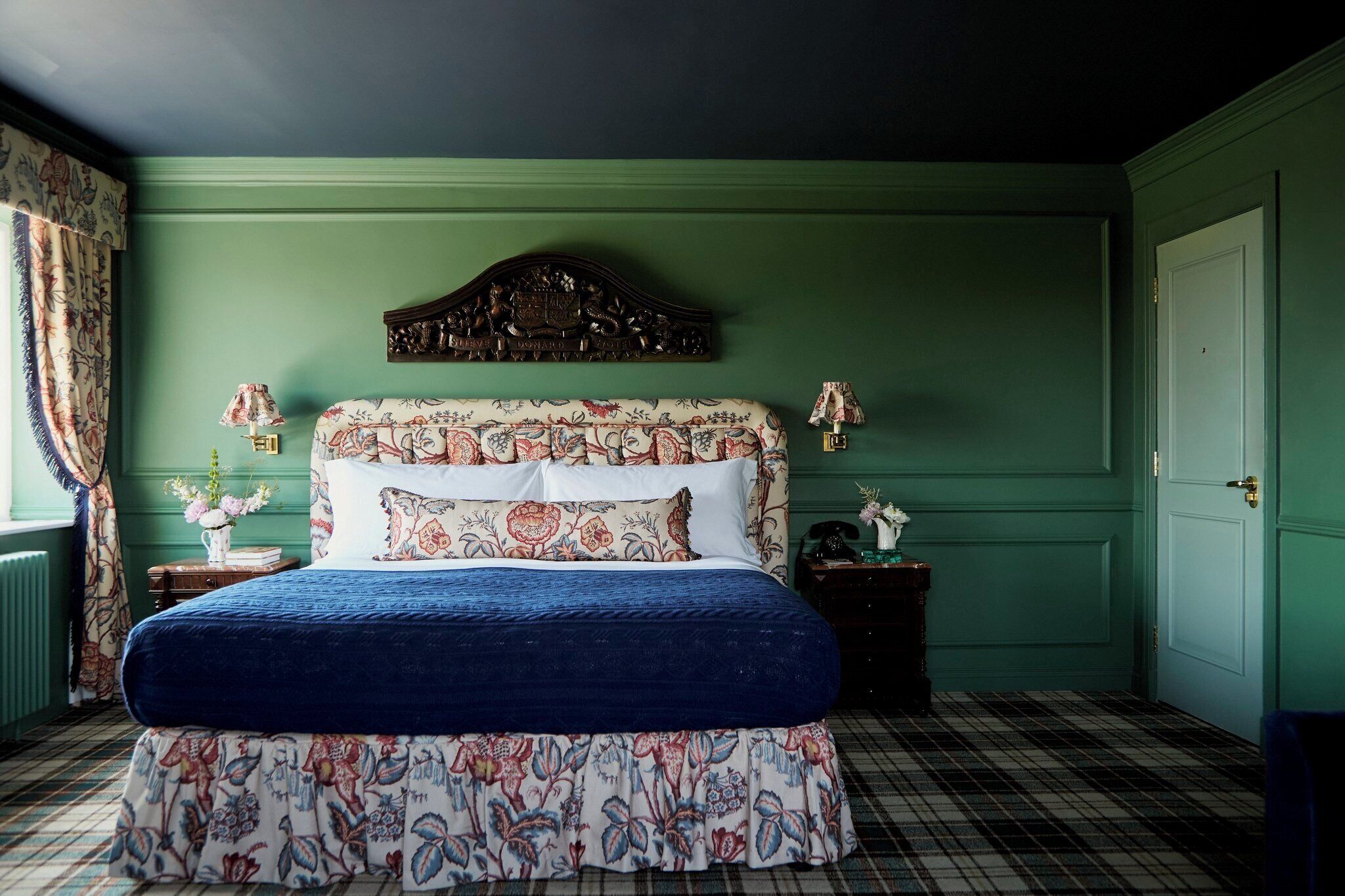 A bedroom with a floral bedspread, a headboard with a crest, and a plaid floor.