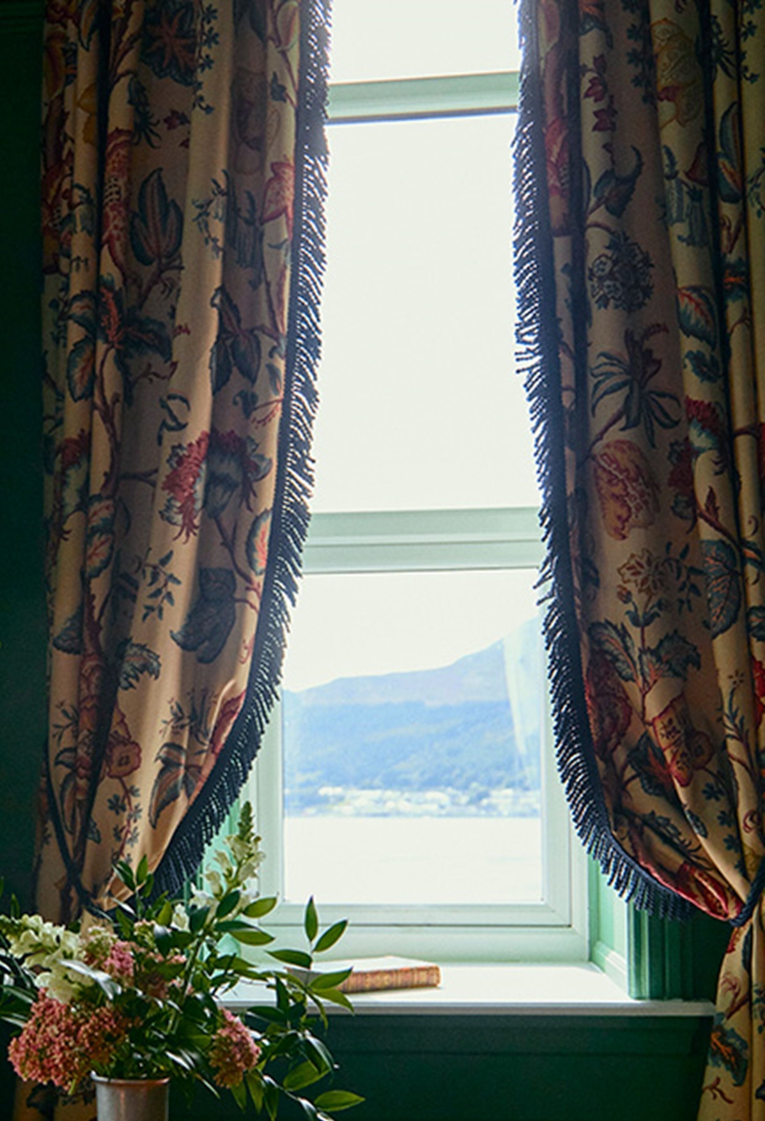 A window with floral curtains and a view of a landscape.