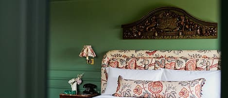 A bedroom with a floral-patterned bedspread, a wooden headboard, and a green wall.