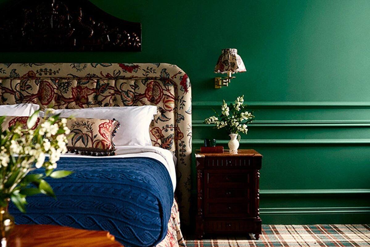 A bedroom with a bed, a nightstand, a lamp, and a floral-patterned chair.