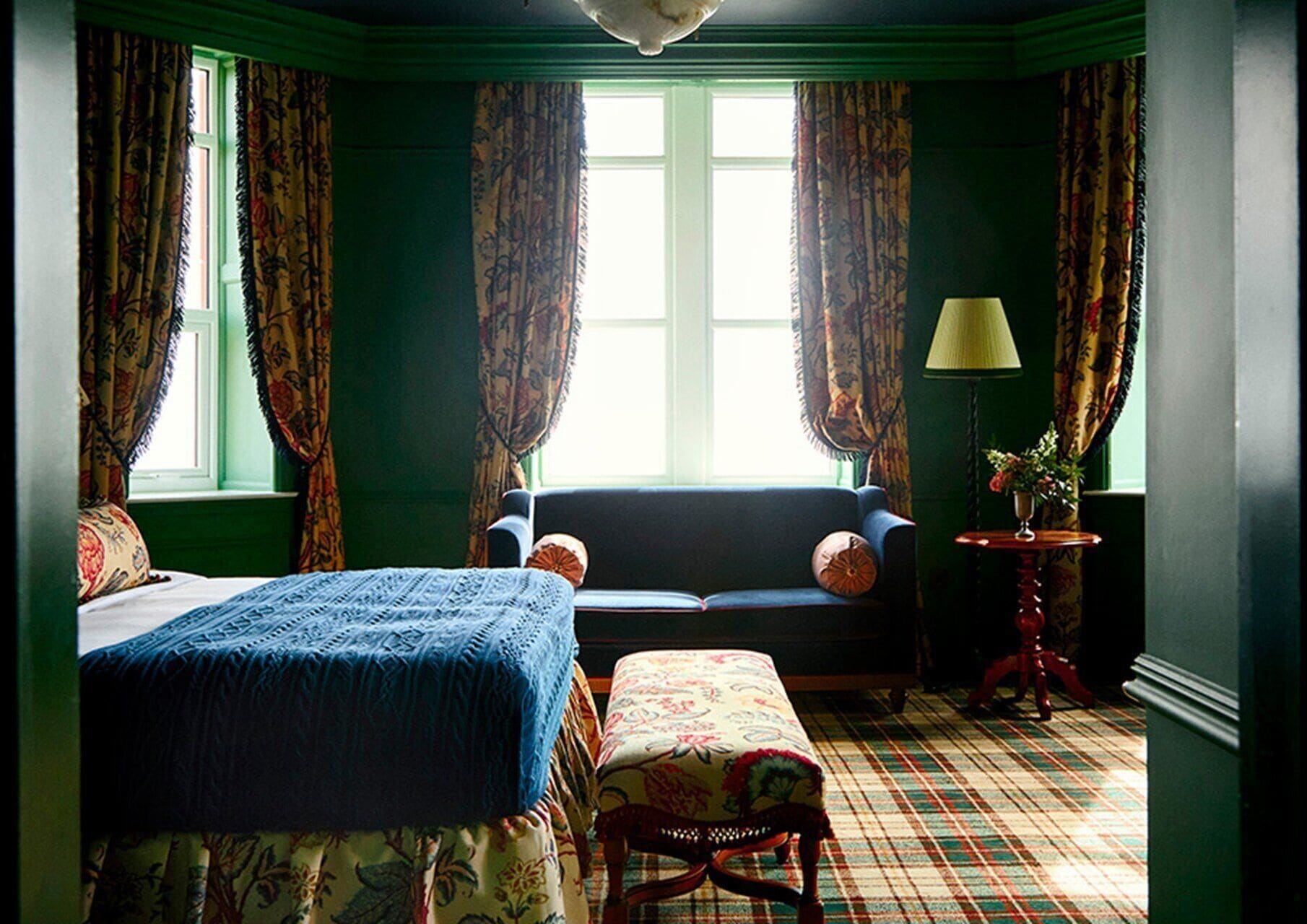 A room with a bed, a sofa, a chair, a lamp, and a window with curtains.