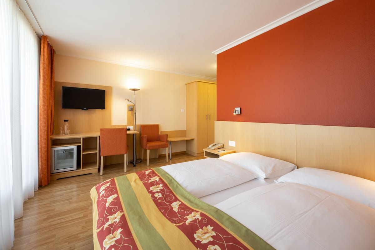 Una habitación de hotel con una cama, un escritorio con una silla, un televisor y un armario.