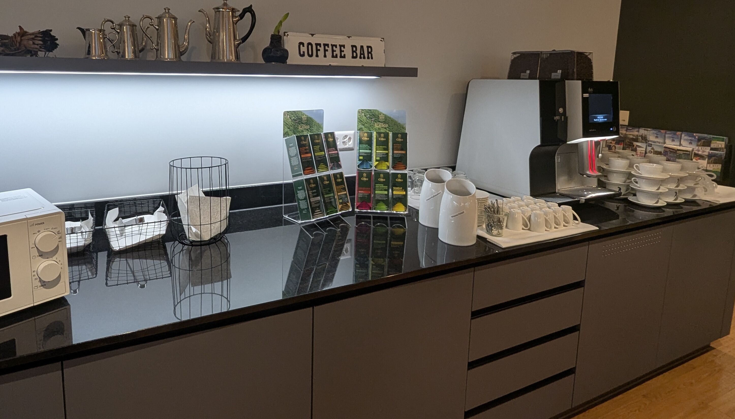 Una cafetería con una máquina de café, un molinillo y una exposición de cápsulas de café.