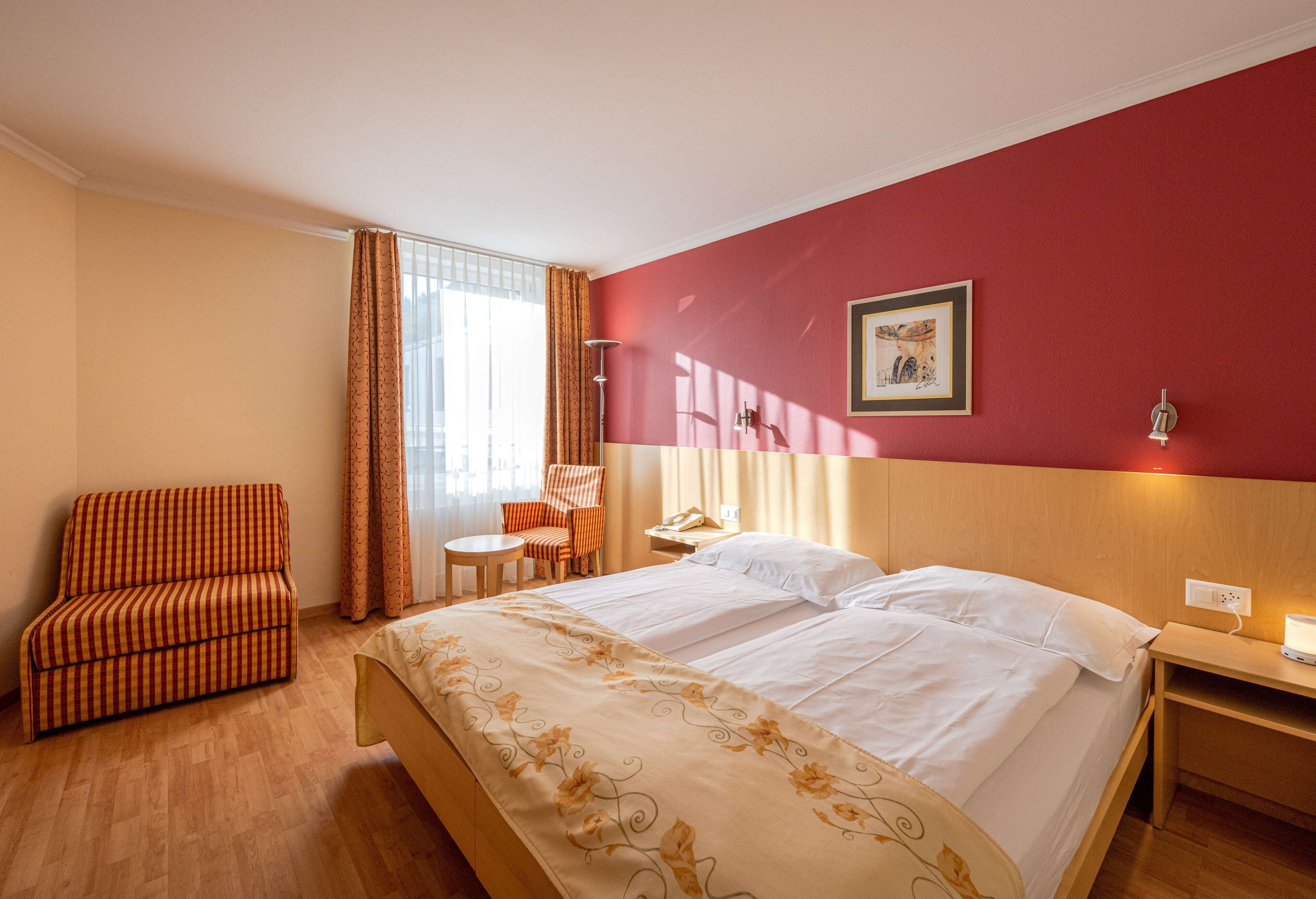 Une chambre d’hôtel comprenant un lit, un canapé, une chaise, une petite table et une table de chevet avec une lampe.
