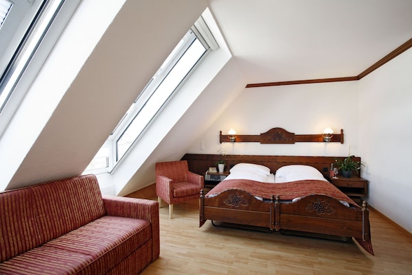 Une chambre avec un plafond en pente, un lit en bois, un canapé rouge recouvert de tissu et une table de chevet avec une lampe.