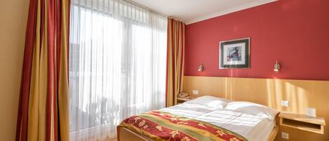 Una habitación de hotel con una cama de madera, una pared decorada en rojo, un cuadro enmarcado y una mesita de noche con una lámpara.