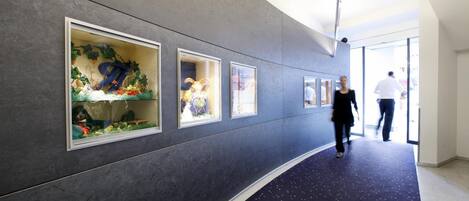A hallway with framed artwork on the walls, a carpeted floor, and a person walking in the distance.