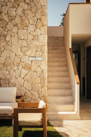 A stone wall, a wooden chair, a white sofa, and a staircase leading to an upper level. - Mavi Suite Türkbükü (Bodrum)
