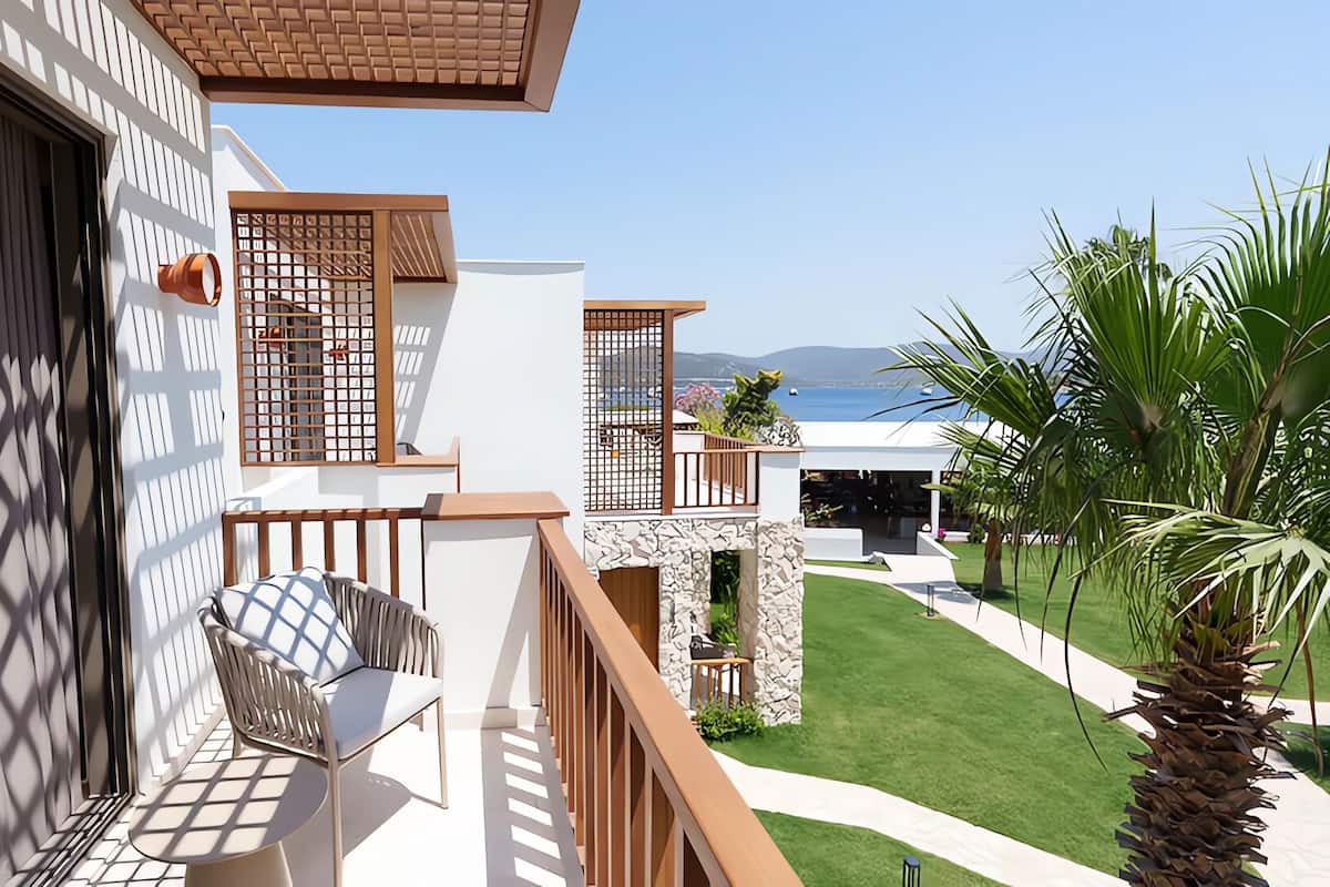 A balcony with a view of the sea, a stone wall, and a palm tree.