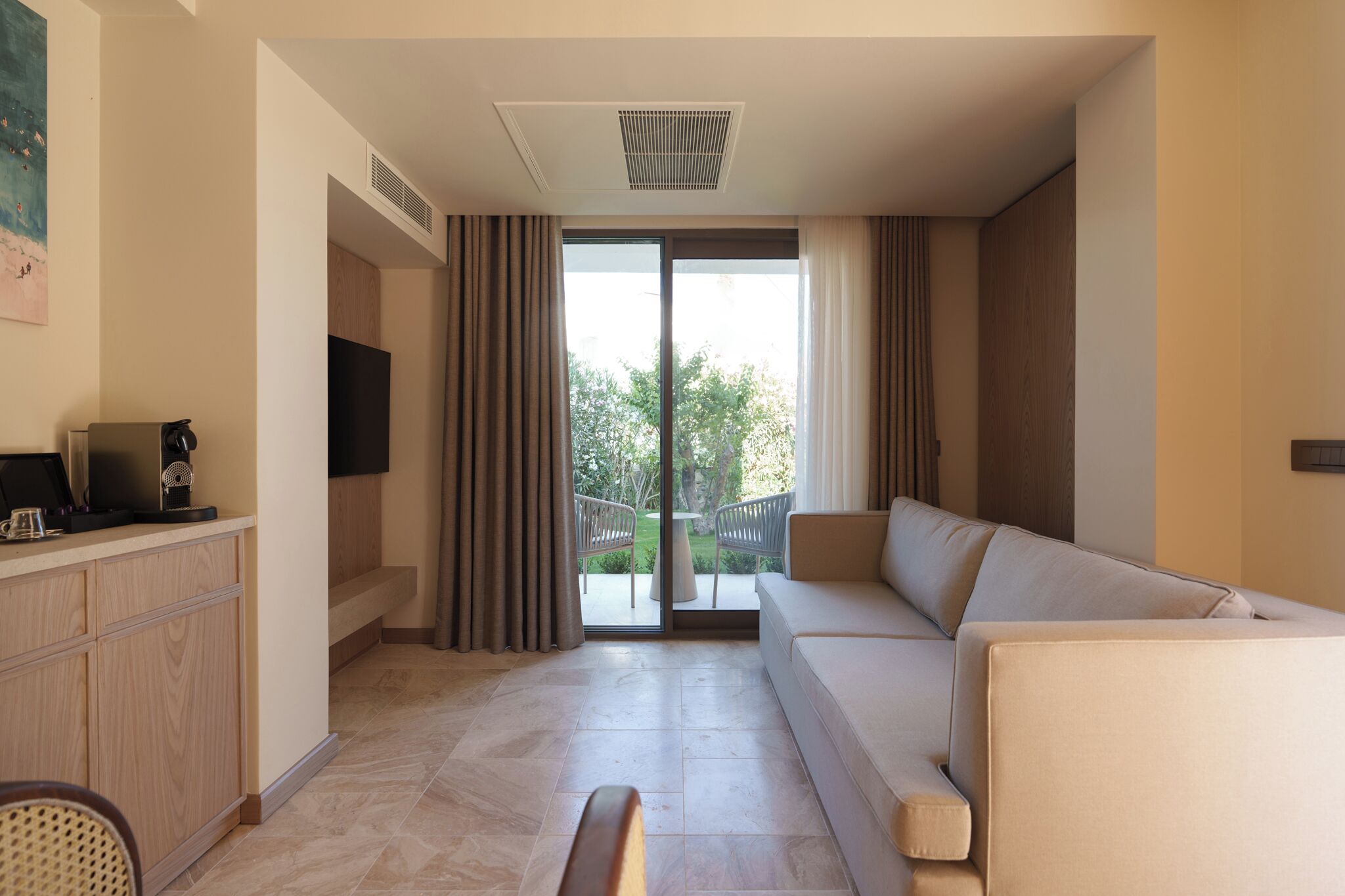 Et moderne hotelværelse med en sofa, et fjernsyn, et skrivebord med en computer og en skydedør til et udendørs område.
