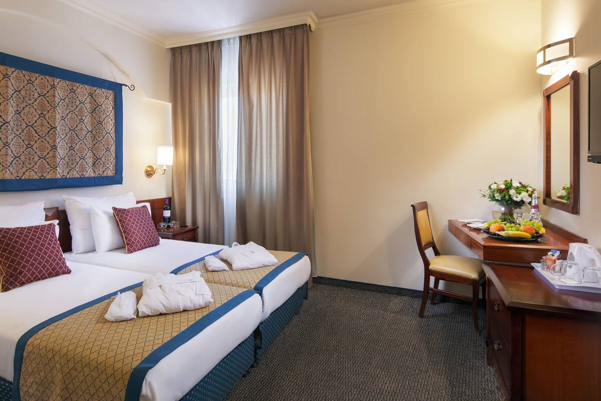 Une chambre d’hôtel avec deux lits, un bureau agrémenté d’un vase de fleurs, une chaise et une grande fenêtre avec des rideaux.